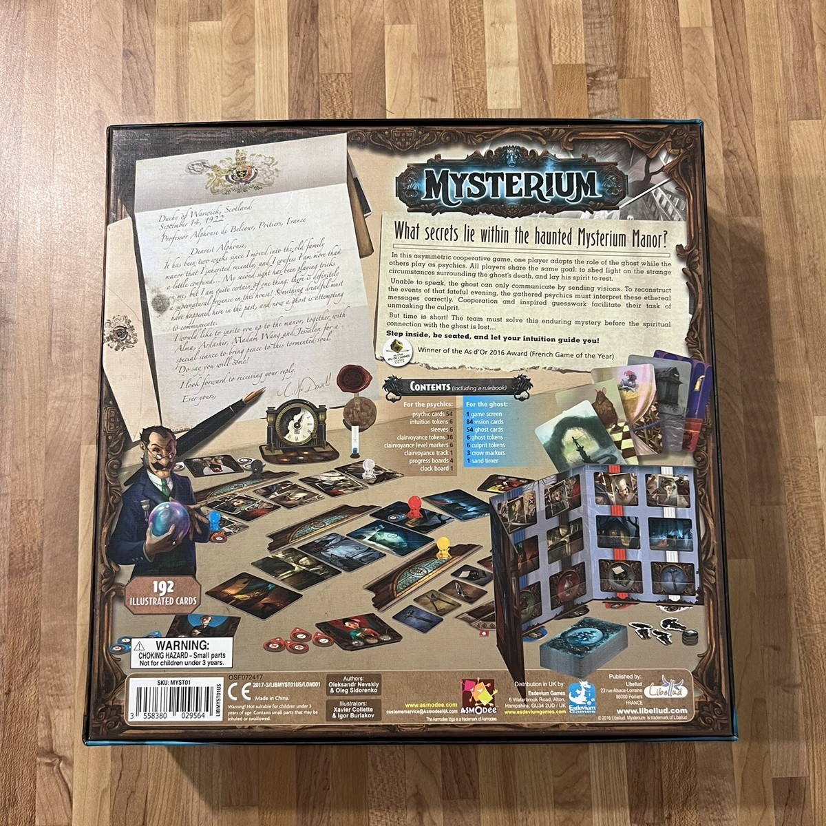 Pudełko gry Mysterium z widmem unoszącym się nad surrealistycznymi wizjami i detektywami