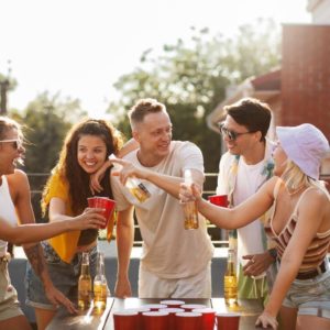 Roześmiana grupa przyjaciół na imprezie gra w różne gry z piwem i toastuje kufle