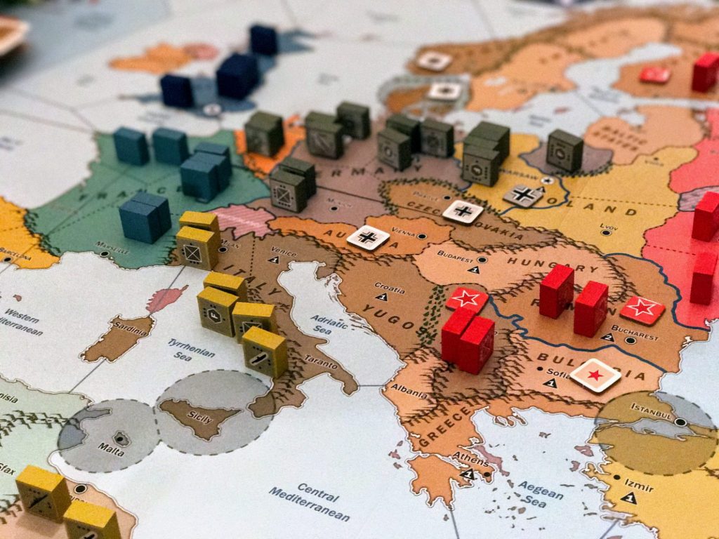 gracze przy stole z dużą planszą gry wojennej pełną figurek żołnierzy